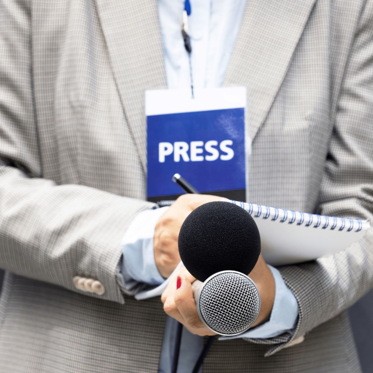 Person in suit with press badge holding a mic and notepad